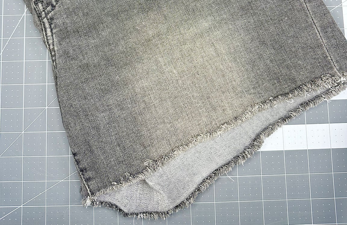 raw hem of jeans laying on cutting mat from tutorial for how to keep raw hem jeans from fraying