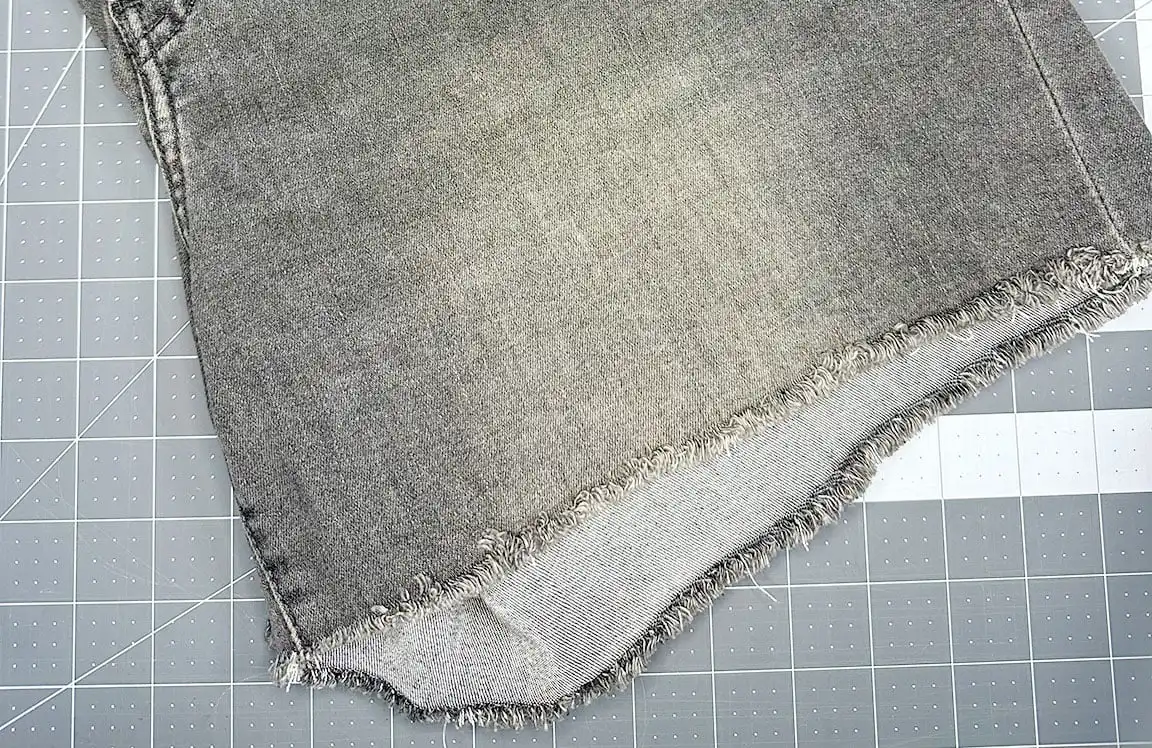 raw hem of jeans laying on cutting mat from tutorial for how to keep raw hem jeans from fraying