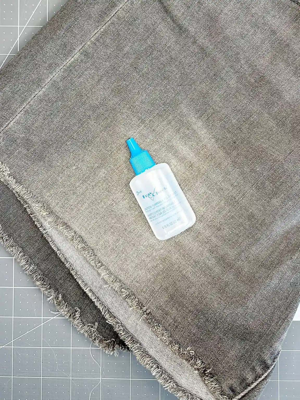 bottle of fray check laying on a pair of raw hem jeans