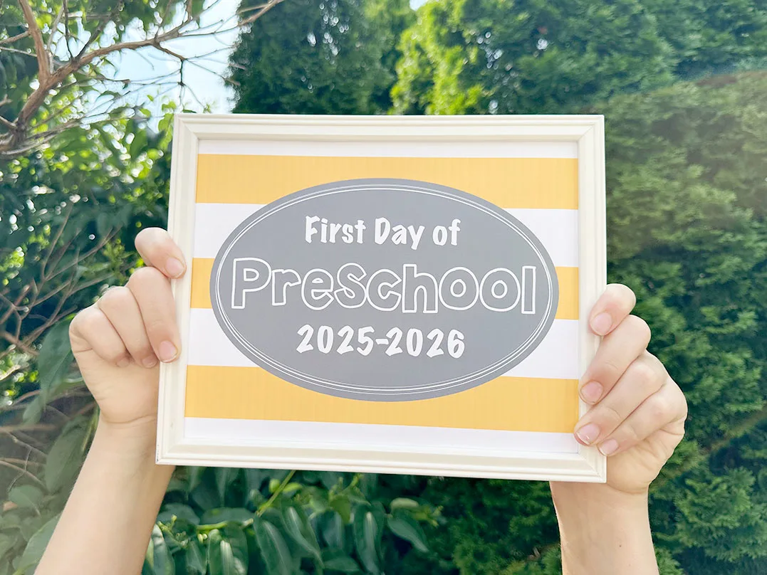 first day of school signs 2025 sign being held in front of bushes