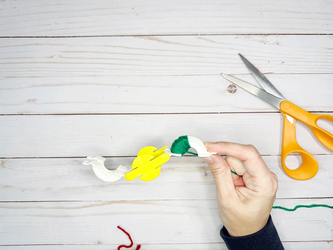 A Pom Pom maker tool wrapped half way across one side with yarn
