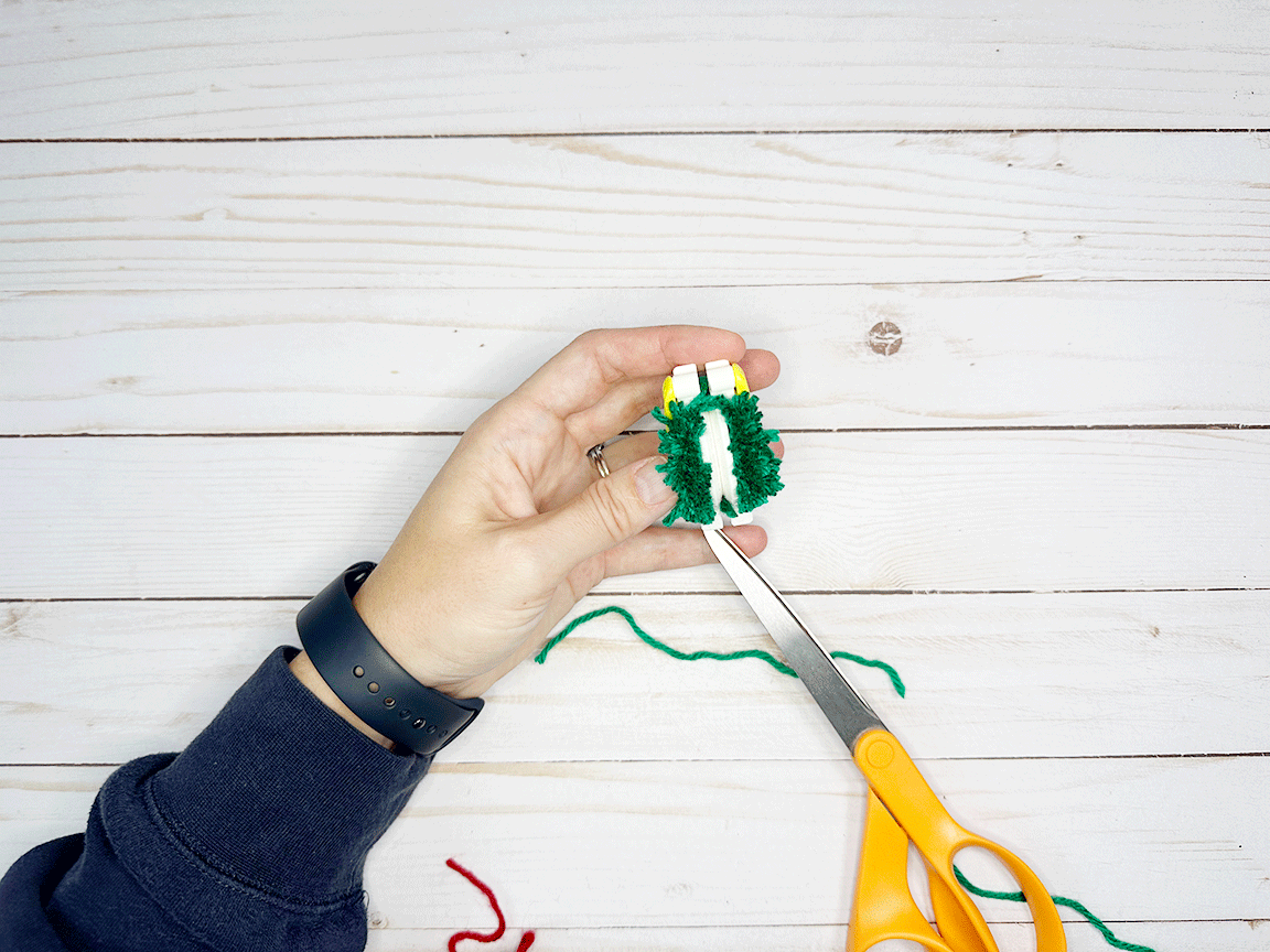 Cutting the yarn along the glove of the Pom Pom maker