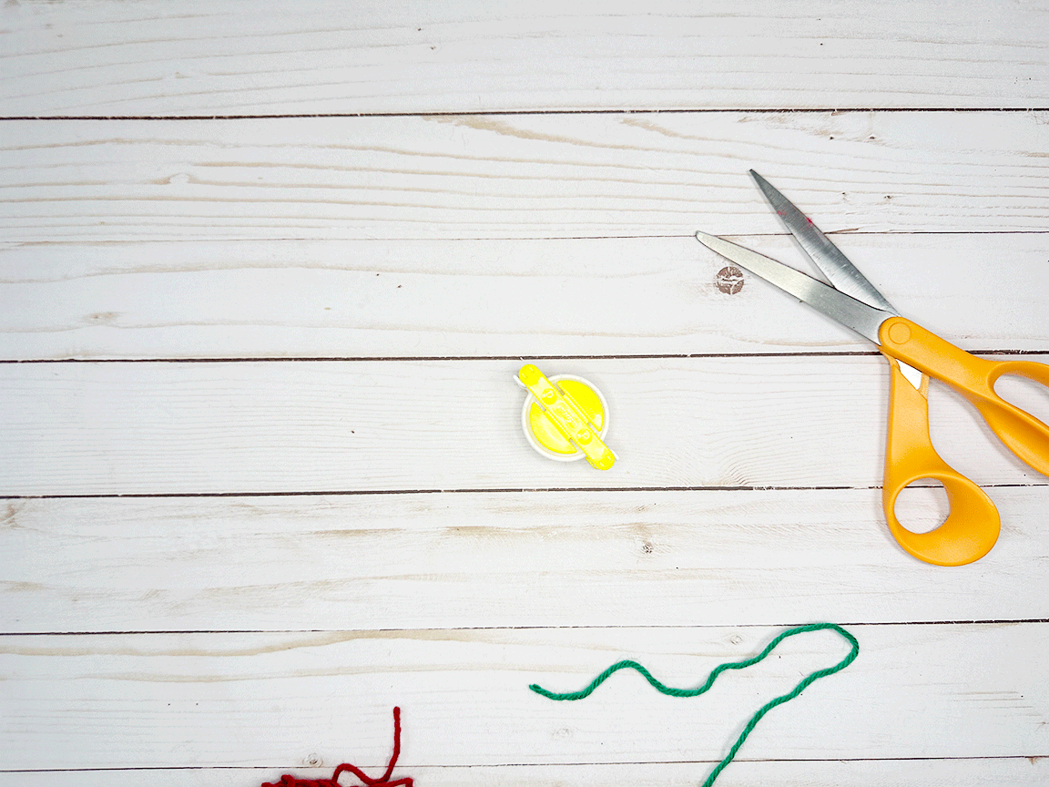 A Pom Pom maker tool sitting on a table with scissors