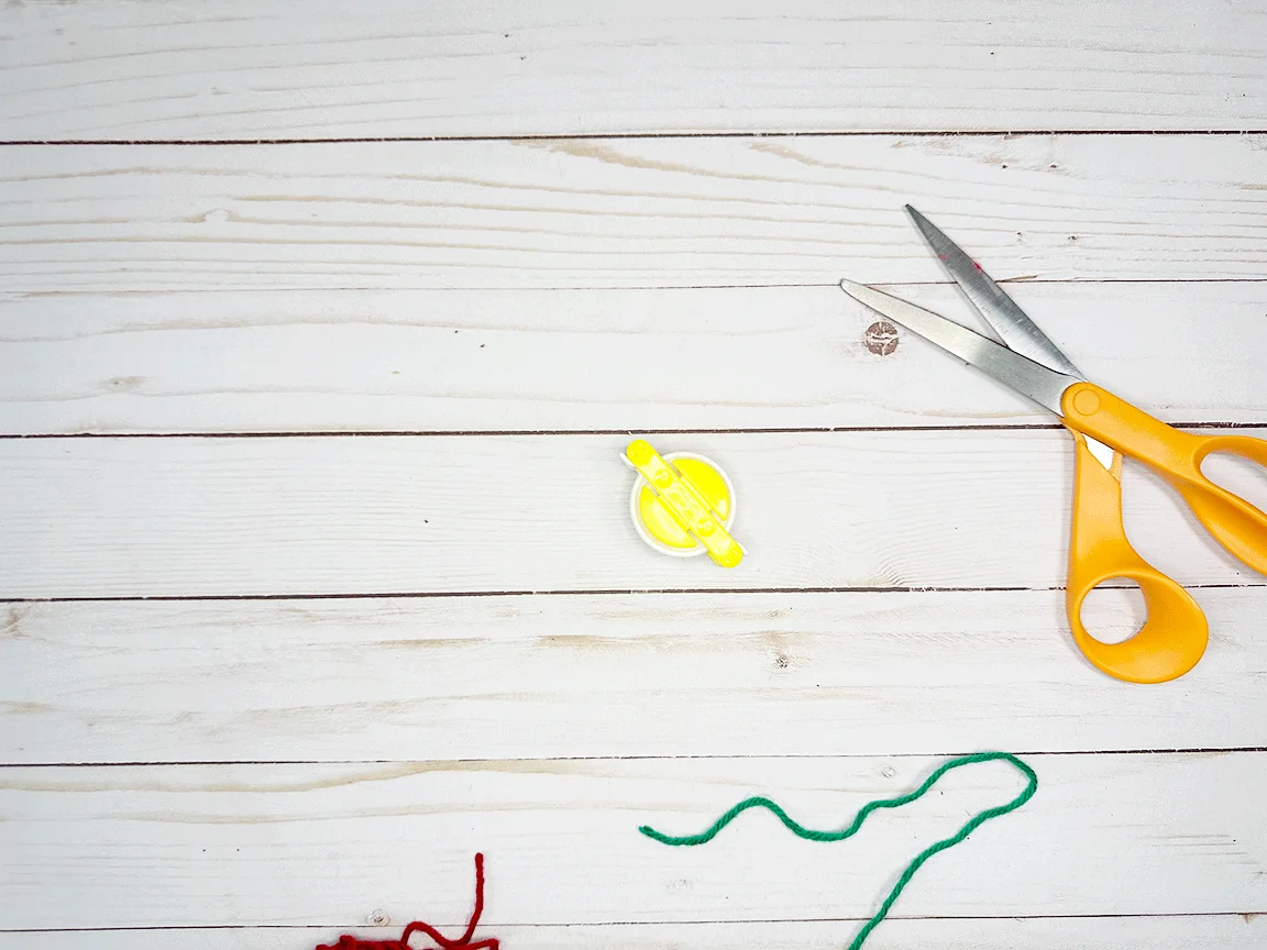 A Pom Pom maker tool sitting on a table with scissors